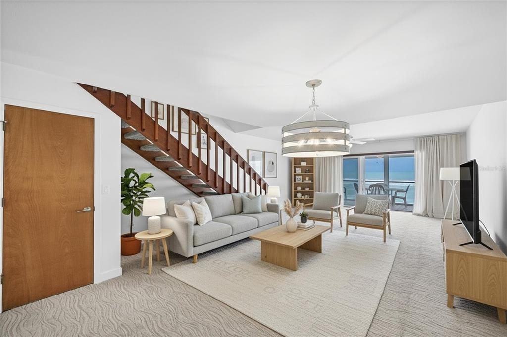 A living room features a wooden staircase, a gray sofa, and a balcony overlooking the ocean — 301 S GULF BOULEVARD UNIT 11, PLACIDA, FL