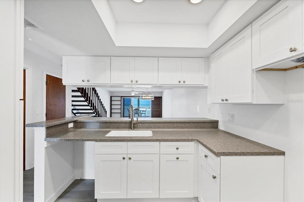 A kitchen features white cabinets, gray countertops, a white sink, and a view of stairs — 301 S GULF BOULEVARD UNIT 11, PLACIDA, FL