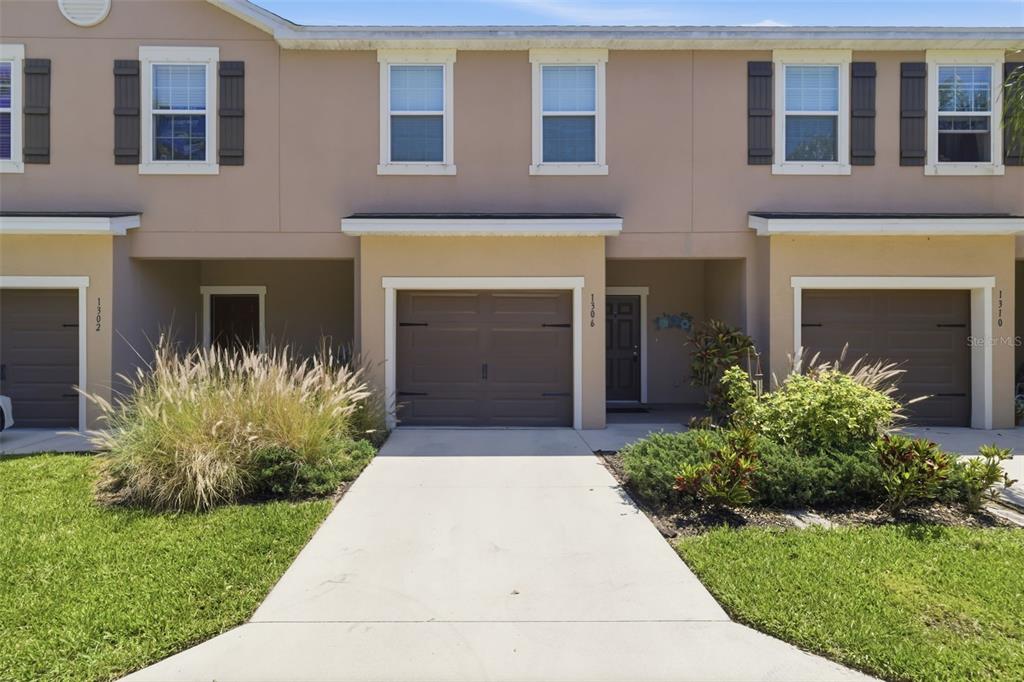 The exterior of a multi-unit townhouse building features beige stucco, brown garage doors, and landscaping — 1306 GRANTHAM DRIVE, SARASOTA, FL