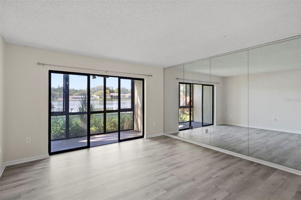 A living room with light wood-look flooring, a mirrored wall, and sliding glass doors to water — 1423 PINE GLEN LANE UNIT C1, TARPON SPRINGS, FL
