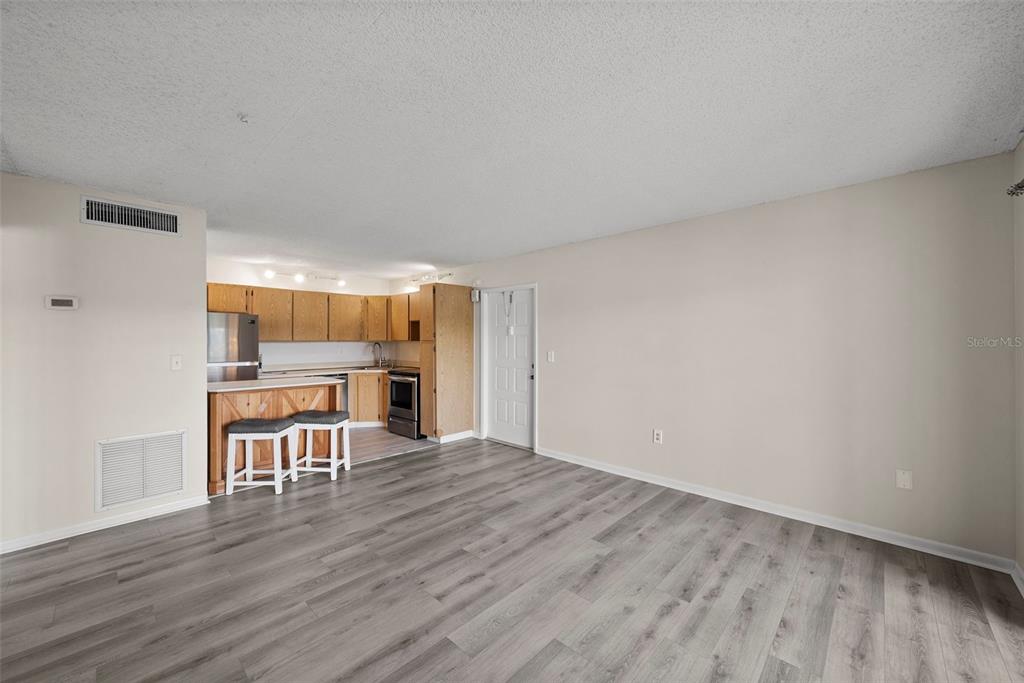 An open-concept living area features wood-look flooring, a kitchen with wooden cabinets, and a breakfast bar — 1423 PINE GLEN LANE UNIT C1, TARPON SPRINGS, FL