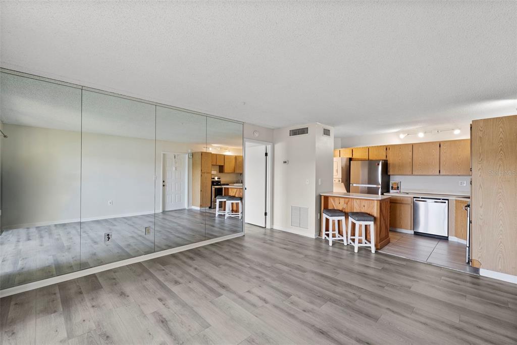A living area with mirrored walls and wood-look flooring opens into a kitchen with bar seating — 1423 PINE GLEN LANE UNIT C1, TARPON SPRINGS, FL