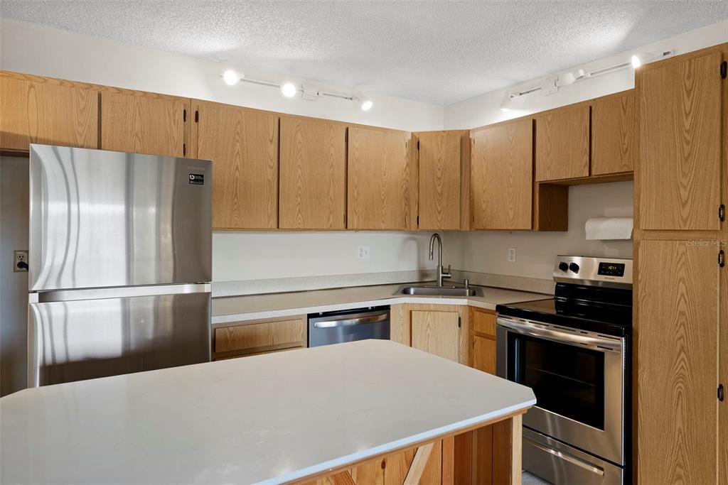 A kitchen features light wood cabinets, stainless steel appliances, and a white countertop island — 1423 PINE GLEN LANE UNIT C1, TARPON SPRINGS, FL