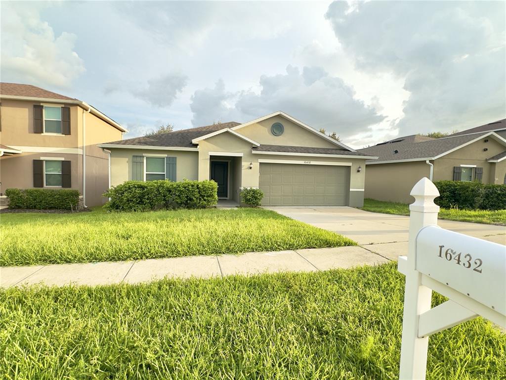 A single-story suburban house with a tan exterior, a two-car garage, and a white mailbox — 16432 CAJU ROAD, CLERMONT, FL