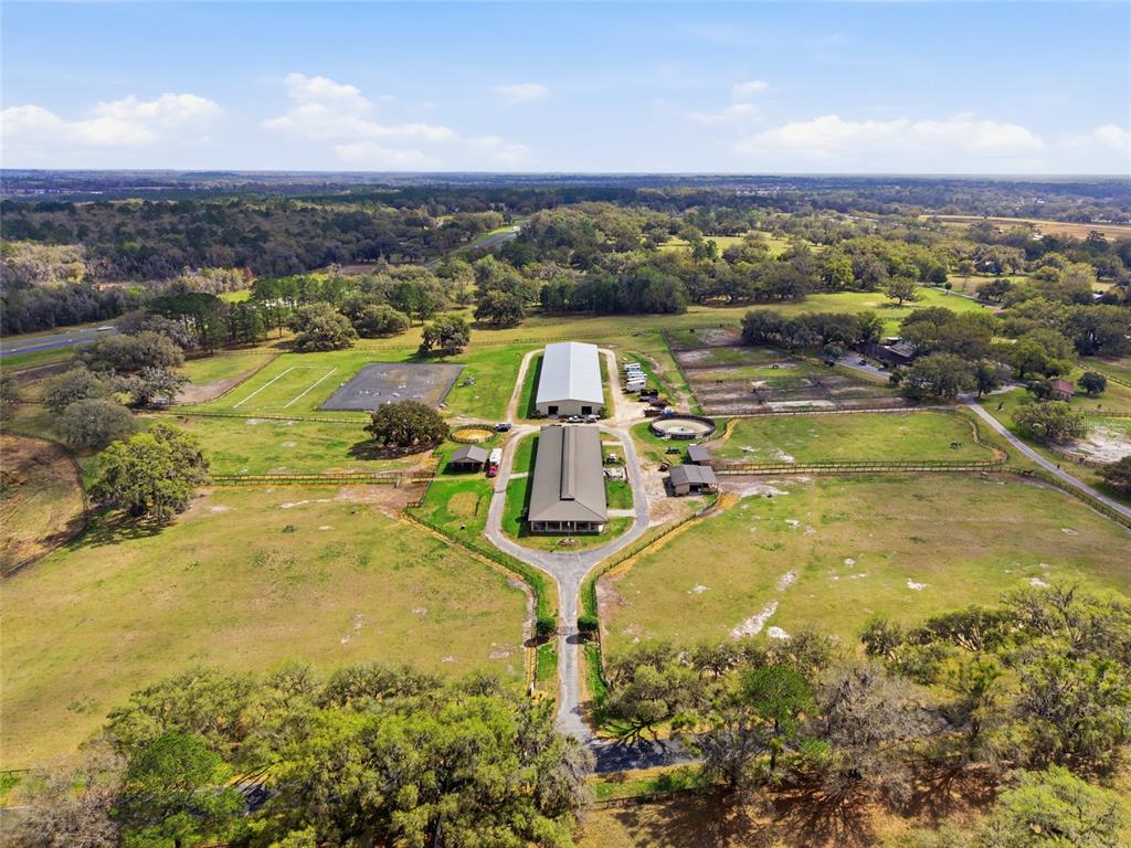An aerial view shows a rural equestrian property with two large barns and fenced pastures — 6025 NW 115TH AVENUE, OCALA, FL