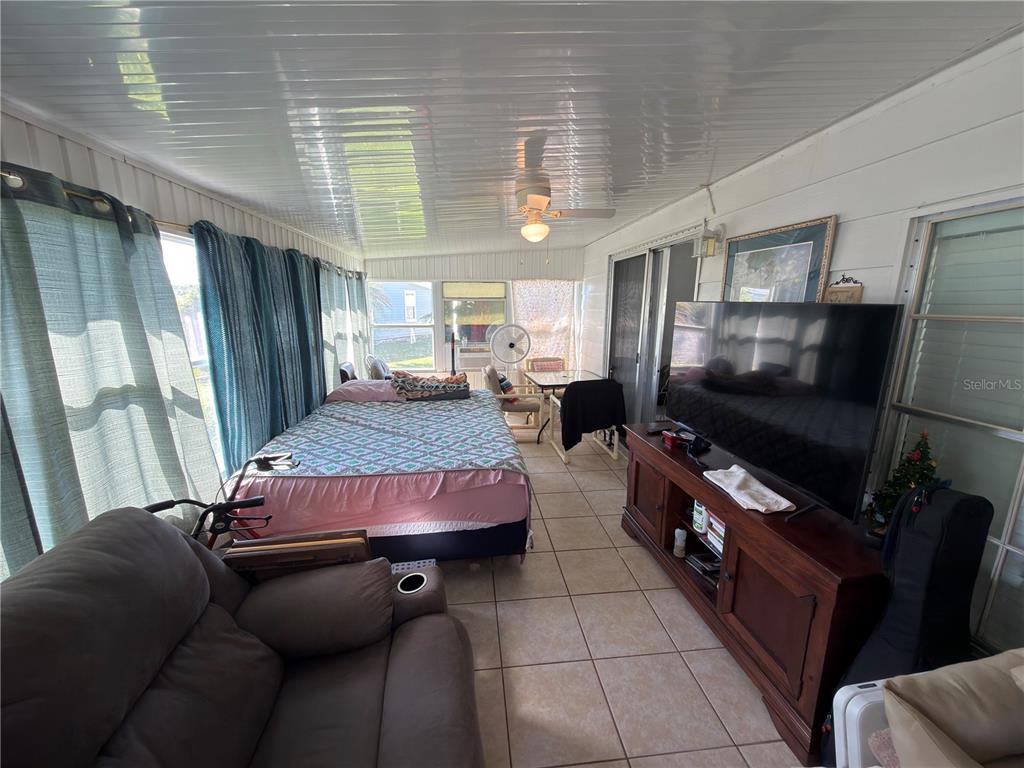 A sunroom features tile flooring, a bed, a television on a wooden stand, and curtains — 2055 S FLORAL AVENUE UNIT 42, BARTOW, FL