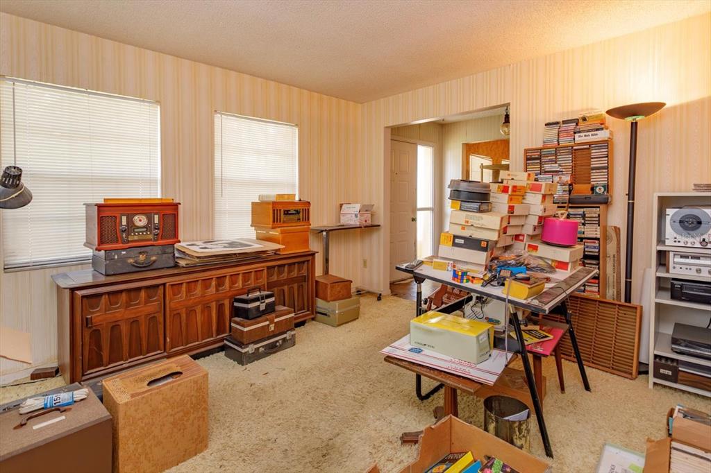 A cluttered room features striped wallpaper, beige carpeting, vintage electronics, and stacks of boxes — 1016 CATHY DRIVE, ALTAMONTE SPRINGS, FL