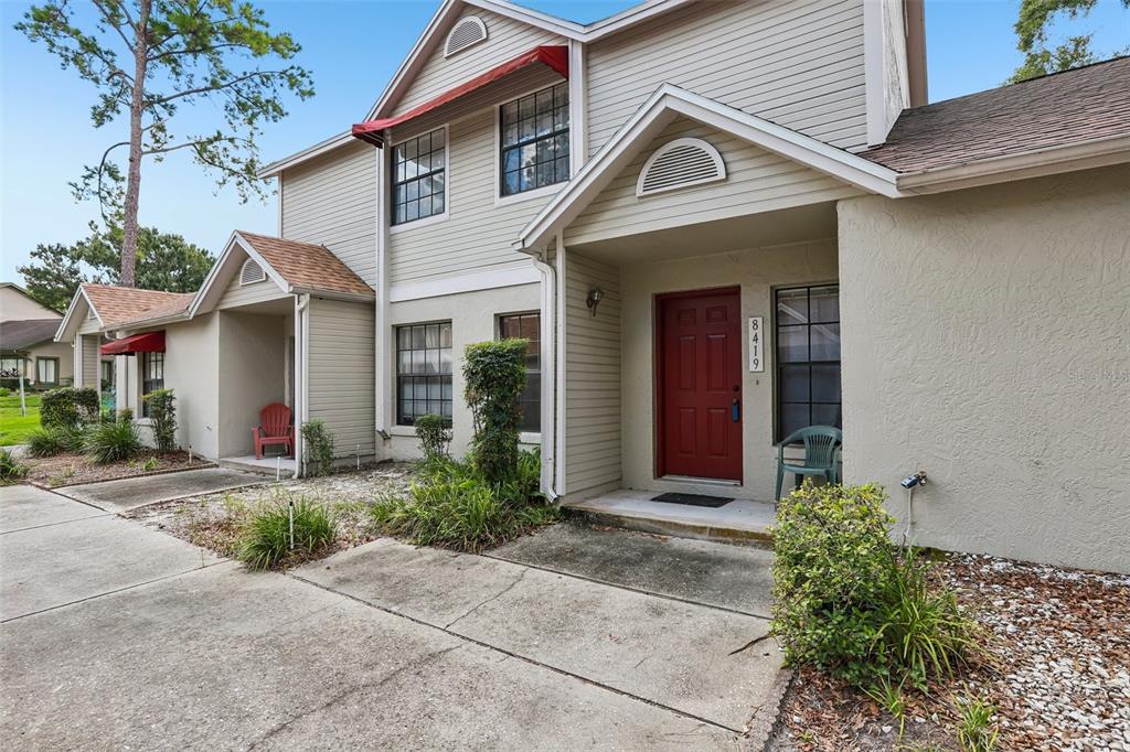 A two-story house with beige siding, a red front door, and red window awnings — 8419 LAURELON PLACE, TEMPLE TERRACE, FL