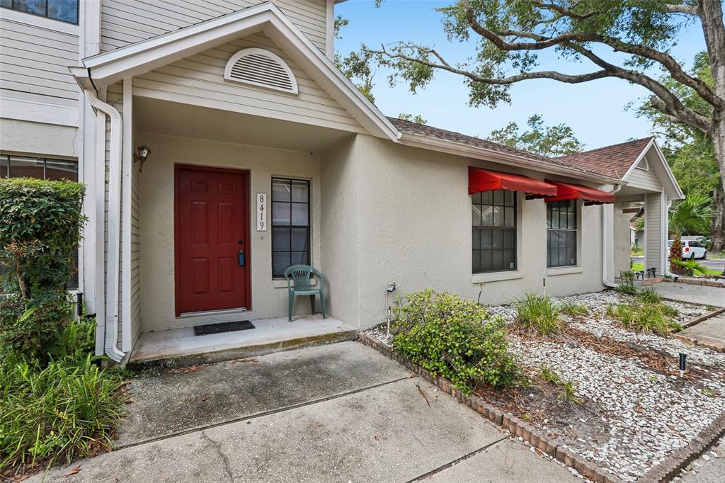 A two-story townhouse exterior features beige siding, a red front door, and red window awnings — 8419 LAURELON PLACE, TEMPLE TERRACE, FL