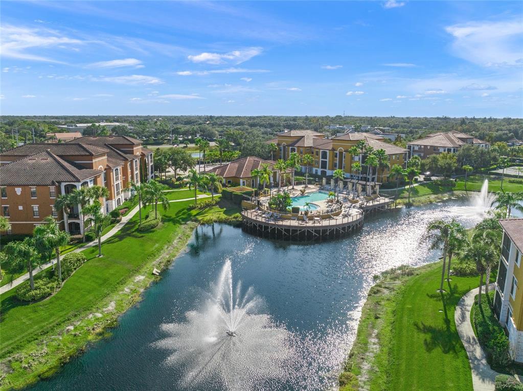 An aerial view of an apartment complex featuring a lake with fountains and a pool — 8341 38TH STREET CIRCLE E UNIT 303, SARASOTA, FL