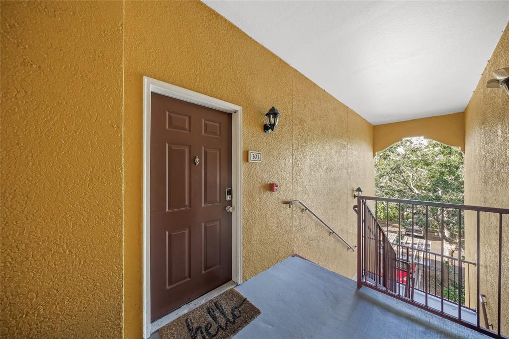 A brown front door with a hello mat is located on an outdoor apartment balcony — 8341 38TH STREET CIRCLE E UNIT 303, SARASOTA, FL