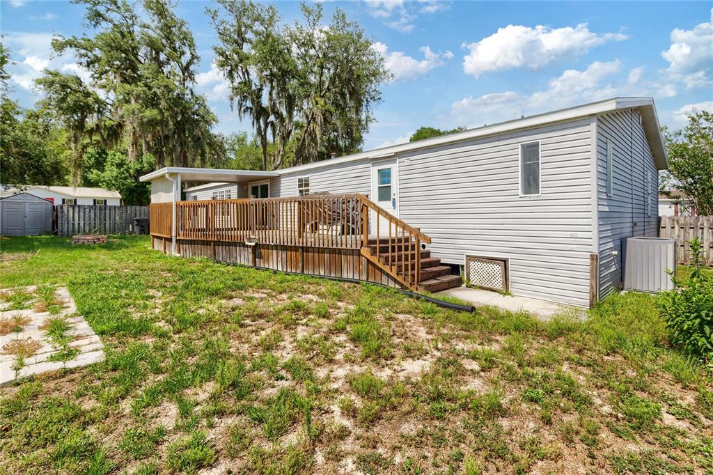 A light gray mobile home features a wooden deck and stairs in a grassy yard — 3518 KIAH DRIVE, WESLEY CHAPEL, FL