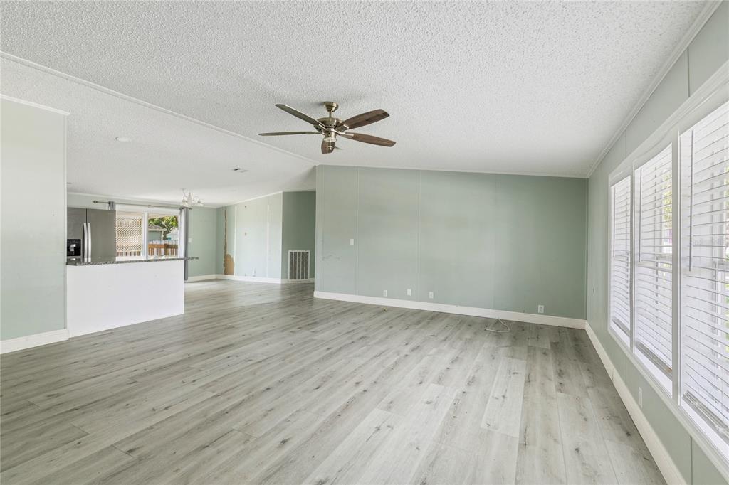 A spacious living room features light wood-look flooring, pale green walls, and a ceiling fan — 3518 KIAH DRIVE, WESLEY CHAPEL, FL