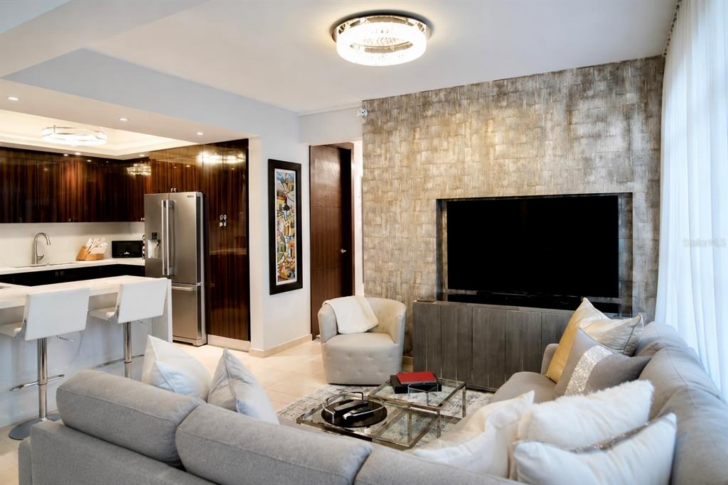 A modern living room with a textured accent wall, a television, and an open kitchen — 405 COND. MIRADOR DEL PARQUE UNIT 904, SAN JUAN, PR