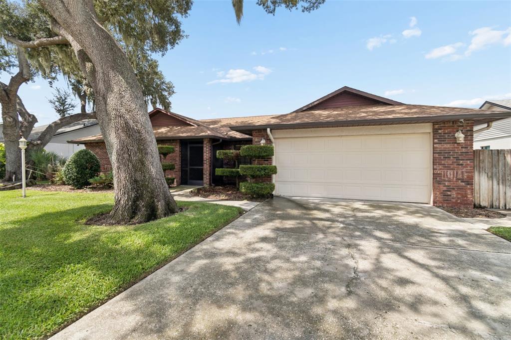 A single-story brick house with a two-car garage, a concrete driveway, and large oak trees — 653 TIMBER POND DRIVE, BRANDON, FL