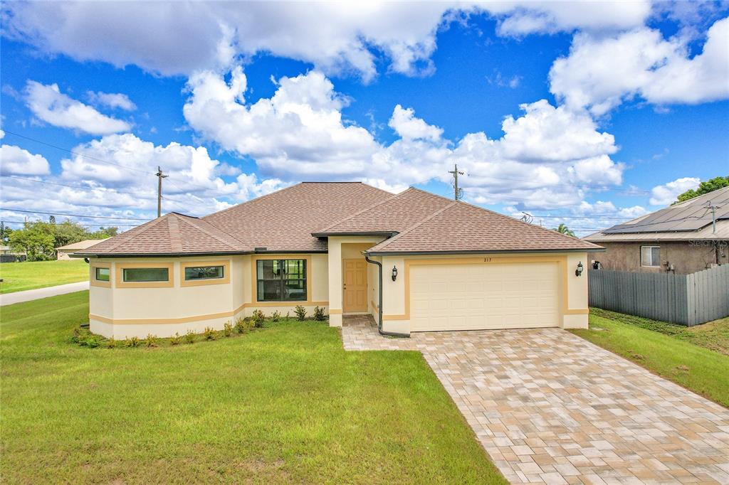 A single-story house with a tan stucco exterior, a hip roof, and a paved driveway — 217 NE 20TH TERRACE, CAPE CORAL, FL