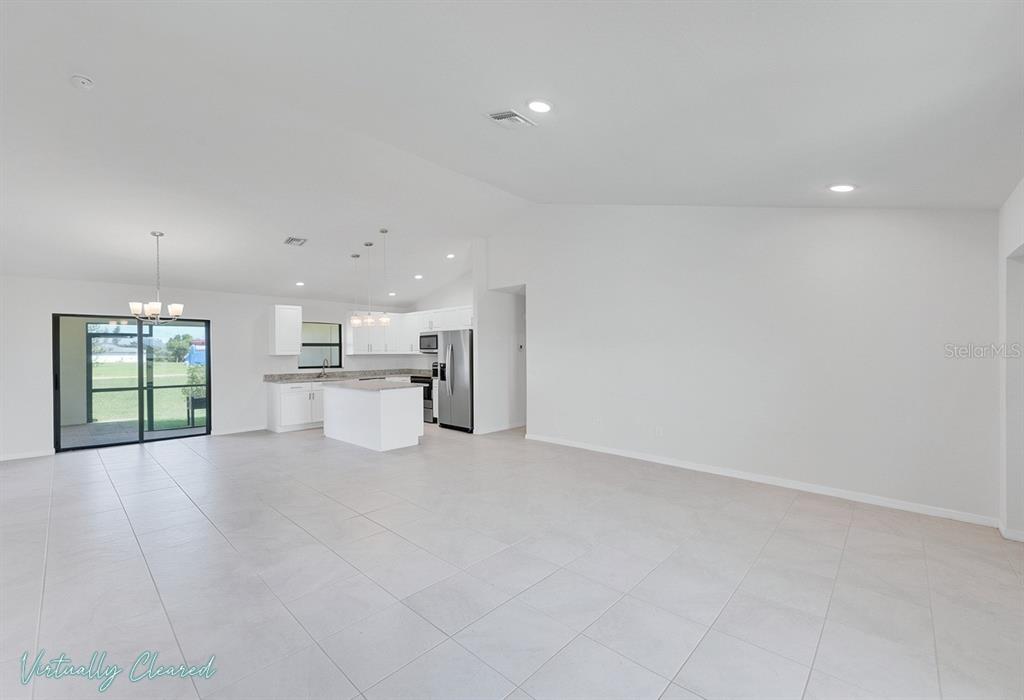 An open-concept kitchen and living area features white cabinetry, tile flooring, and sliding glass doors — 217 NE 20TH TERRACE, CAPE CORAL, FL