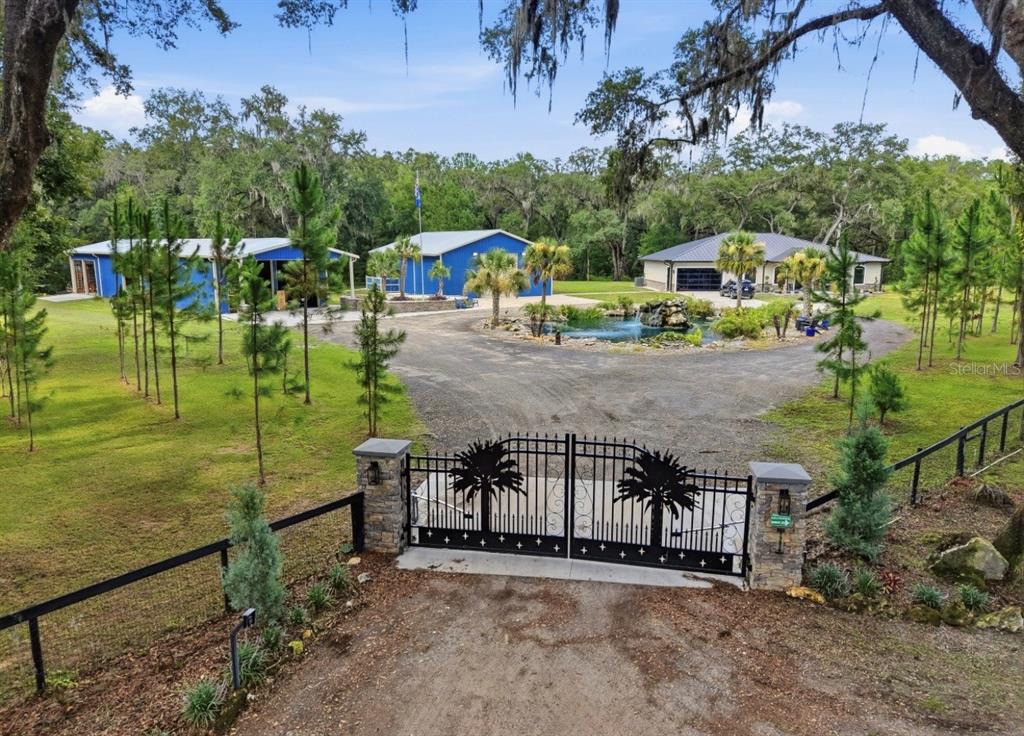 A gated entrance leads to a driveway with a pond and several buildings on wooded land — 19826 NW 6TH AVENUE, NEWBERRY, FL