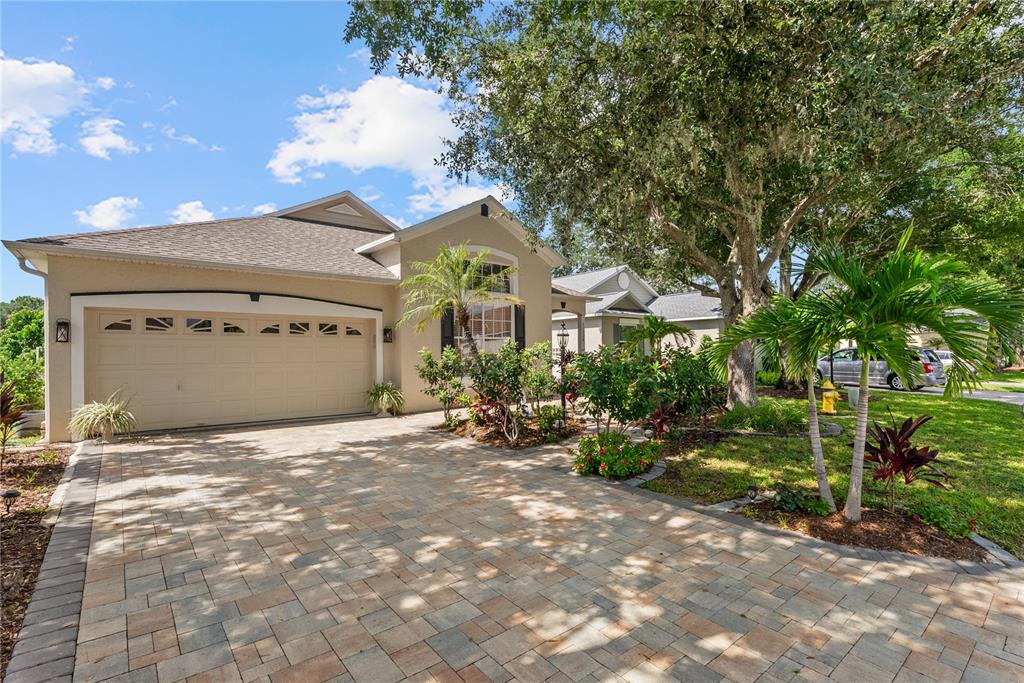 A beige house with a paver driveway, a two-car garage, and mature landscaping — 11326 BLUE SAGE PLACE, LAKEWOOD RANCH, FL