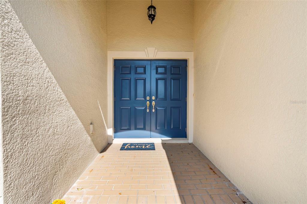 A covered entryway features a brick-tiled floor and blue double doors under a hanging lantern — 29232 COHARIE LOOP, SAN ANTONIO, FL