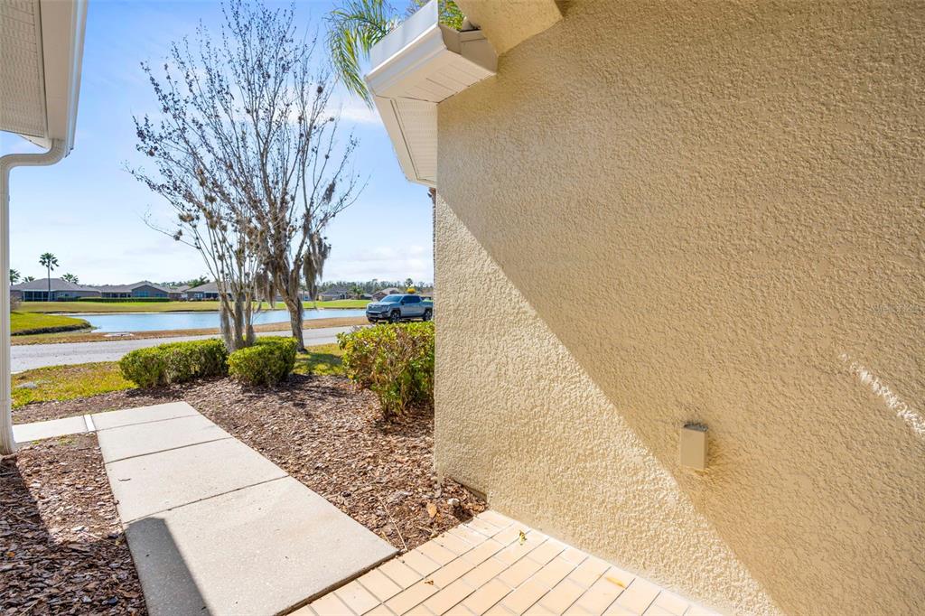 A view of a concrete walkway leading toward a pond beside a stucco house exterior — 29232 COHARIE LOOP, SAN ANTONIO, FL