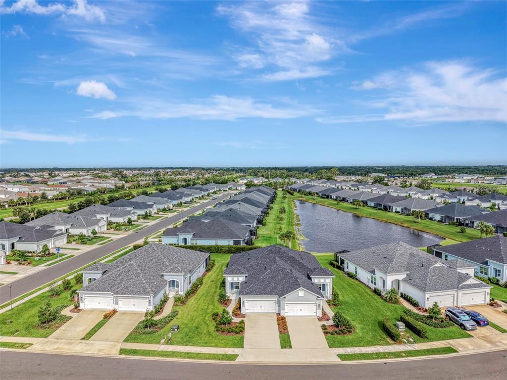 An aerial view of a suburban neighborhood featuring single-story houses, manicured lawns, and a pond — 4842 WILLOW BEND AVENUE, PARRISH, FL