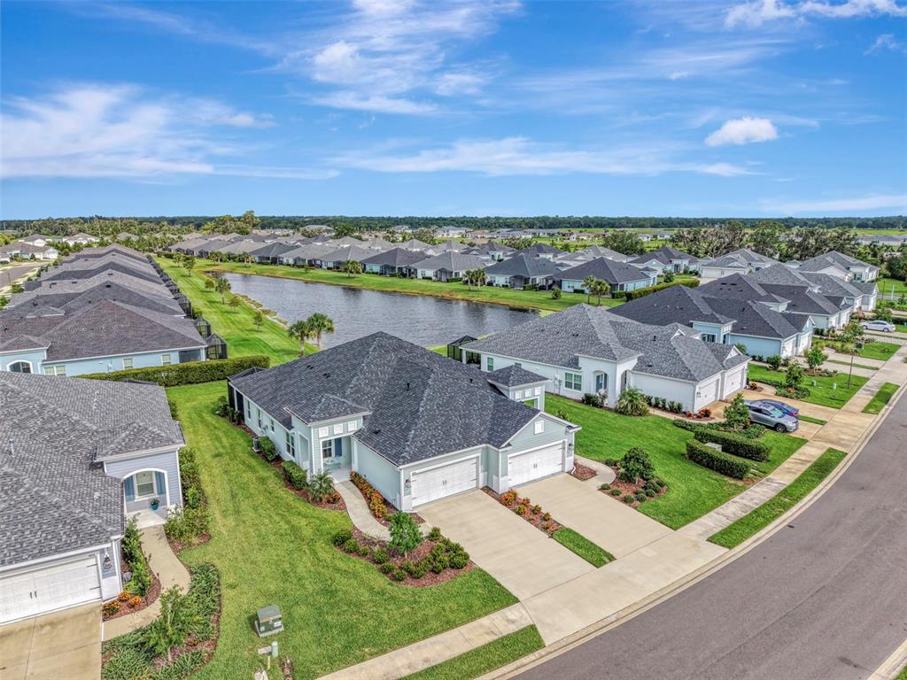 An aerial view shows suburban houses with gray roofs and green lawns near a pond — 4842 WILLOW BEND AVENUE, PARRISH, FL