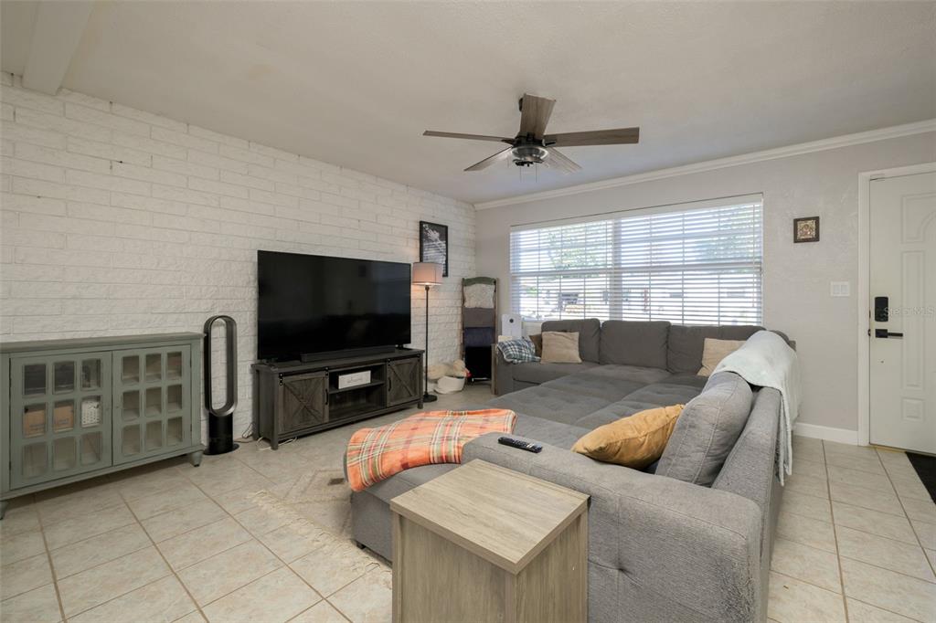 A living room features a white brick wall, gray sectional sofa, and tile flooring — 76 S CAPRI DRIVE, ORMOND BEACH, FL