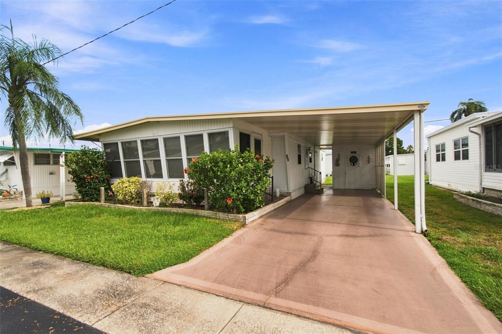 A single-story manufactured home with a carport, a front lawn, and a screened-in porch — 1500 COUNTY ROAD 1 UNIT 107, DUNEDIN, FL