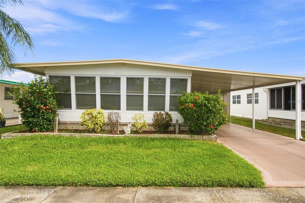 A single-story mobile home with a carport, a front lawn, and a low brick planter — 1500 COUNTY ROAD 1 UNIT 107, DUNEDIN, FL