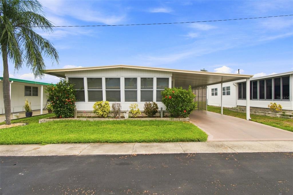 A single-story manufactured home with a screened front porch and an attached carport — 1500 COUNTY ROAD 1 UNIT 107, DUNEDIN, FL