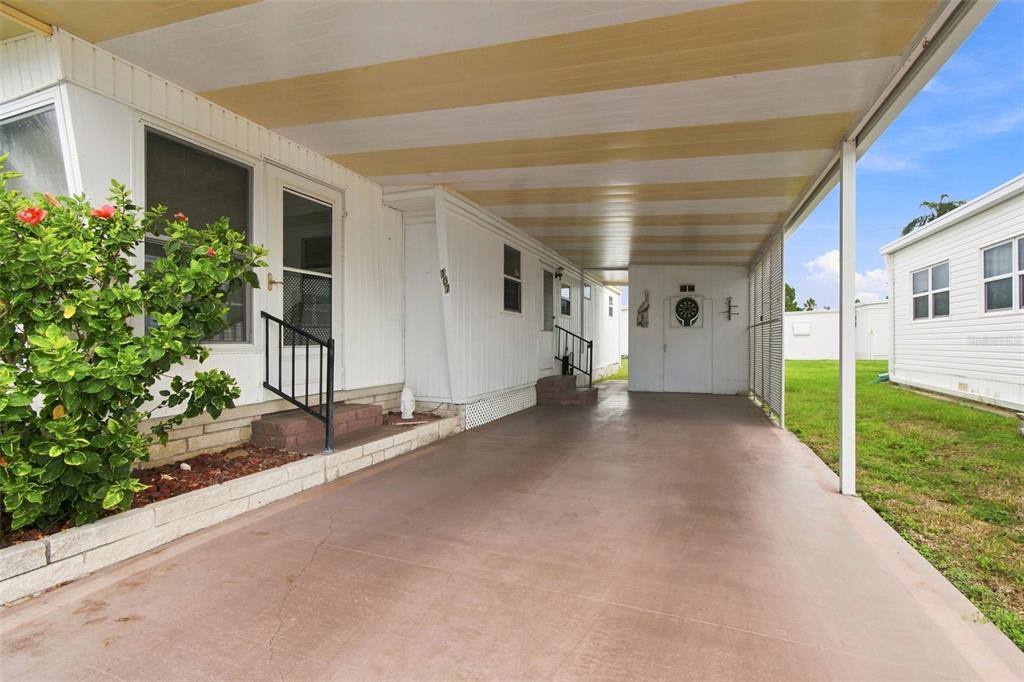 A covered carport with a concrete floor sits beside a white mobile home — 1500 COUNTY ROAD 1 UNIT 107, DUNEDIN, FL