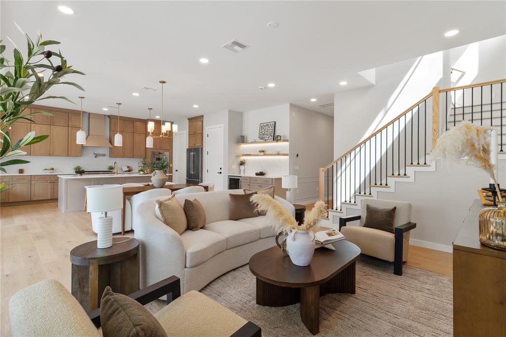 An open-concept living room and kitchen featuring light wood floors, neutral furniture, and a staircase — 516 CLAYTON STREET, ORLANDO, FL