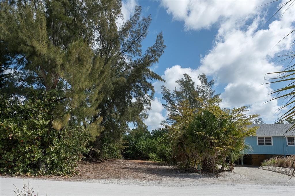 A vacant, sandy lot sits next to a blue house surrounded by trees and foliage — 322 S GULF BOULEVARD, PLACIDA, FL