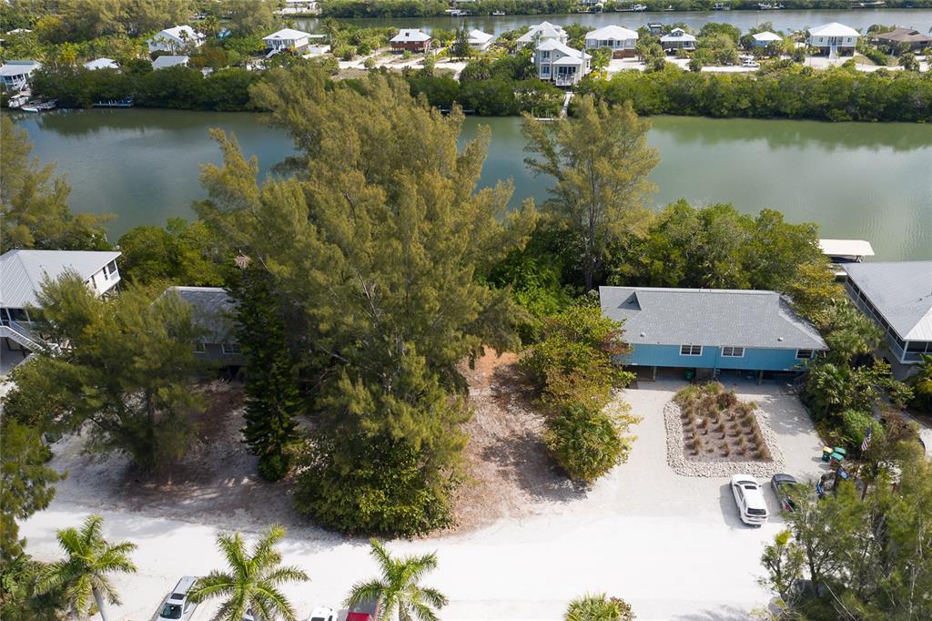 An aerial view shows a waterfront lot with trees, a blue house, and a gravel driveway — 322 S GULF BOULEVARD, PLACIDA, FL