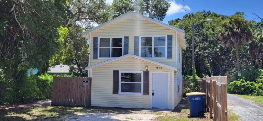 A two-story, light yellow vinyl-sided house with a front door and a blue trash bin — 915 SEMINOLE STREET, CLEARWATER, FL