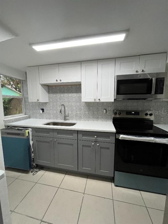 A kitchen features white upper cabinets, gray lower cabinets, a patterned backsplash, and stainless appliances — 915 SEMINOLE STREET, CLEARWATER, FL