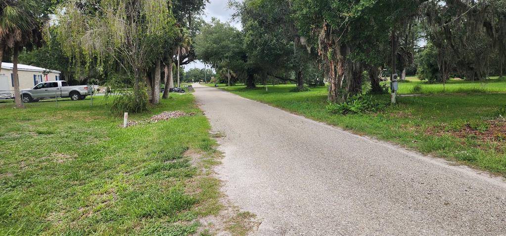 A gravel road runs through a grassy, tree-lined residential area with a parked pickup truck — 1821 LOS PINOS ROAD, ARCADIA, FL