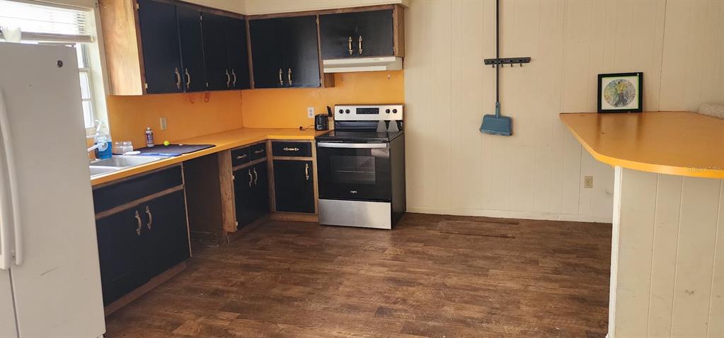 A kitchen features black cabinets, yellow countertops, a stainless steel stove, and wood-look flooring — 1821 LOS PINOS ROAD, ARCADIA, FL