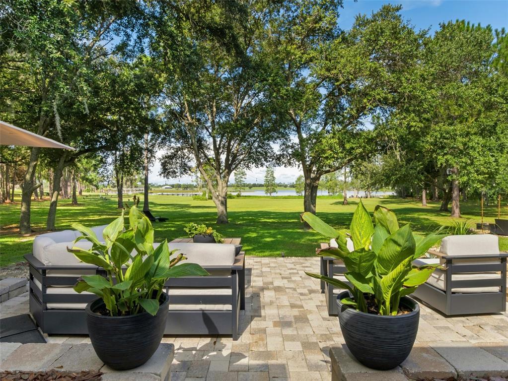 A patio with outdoor seating and potted plants overlooks a large grassy lawn and lake — 12703 MONTEVISTA ROAD, CLERMONT, FL