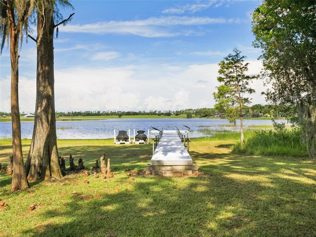 A vibrant sunset glows over a grassy lawn and a lake framed by two large trees — 12703 MONTEVISTA ROAD, CLERMONT, FL