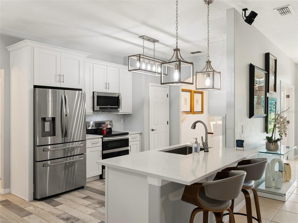 A modern kitchen features white cabinetry, a central island with bar seating, and a dining area — 12703 MONTEVISTA ROAD, CLERMONT, FL