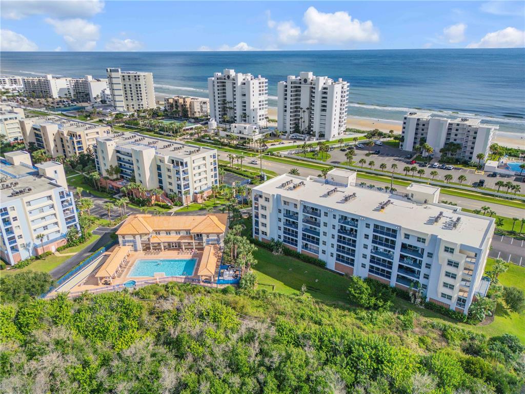 An aerial view shows multiple beachfront condominium buildings, a swimming pool, and surrounding coastal vegetation — 5300 S ATLANTIC AVENUE UNIT 17-207, NEW SMYRNA BEACH, FL