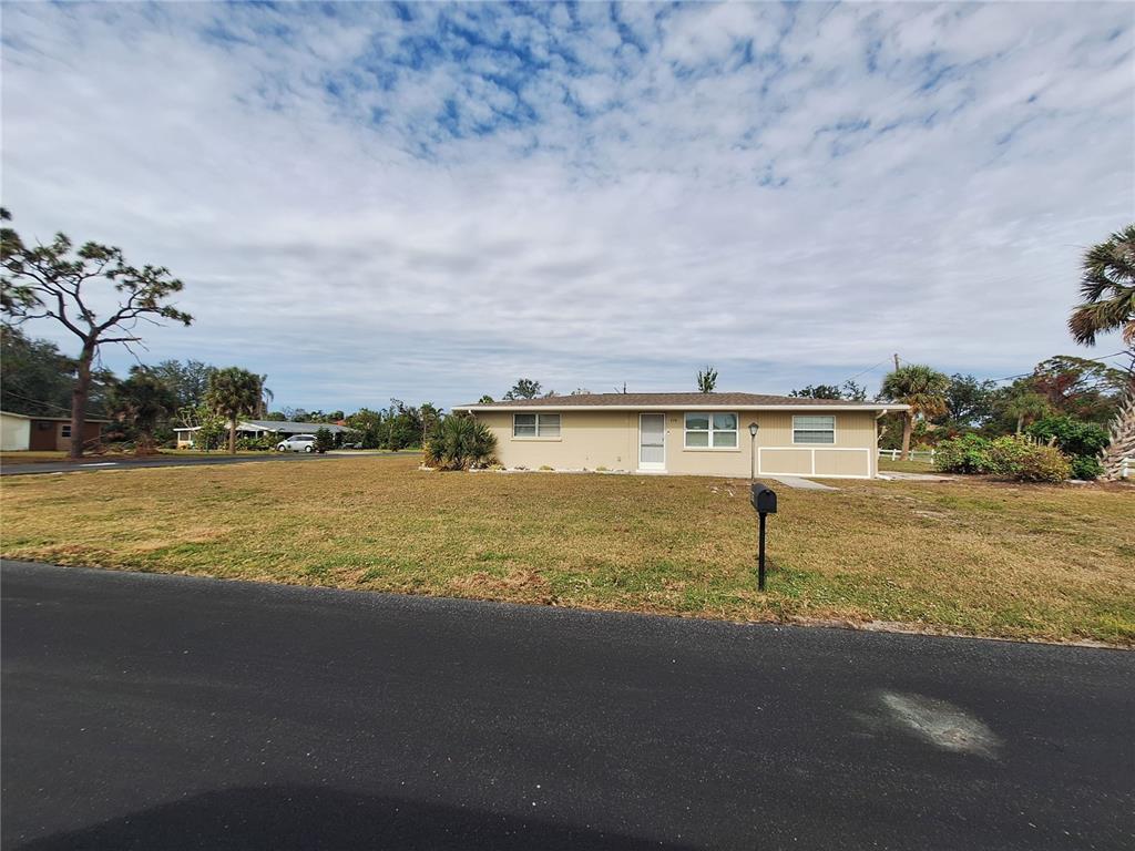 A single-story house with a tan exterior and a paved driveway sits on a lawn — 858 E 7TH STREET, ENGLEWOOD, FL