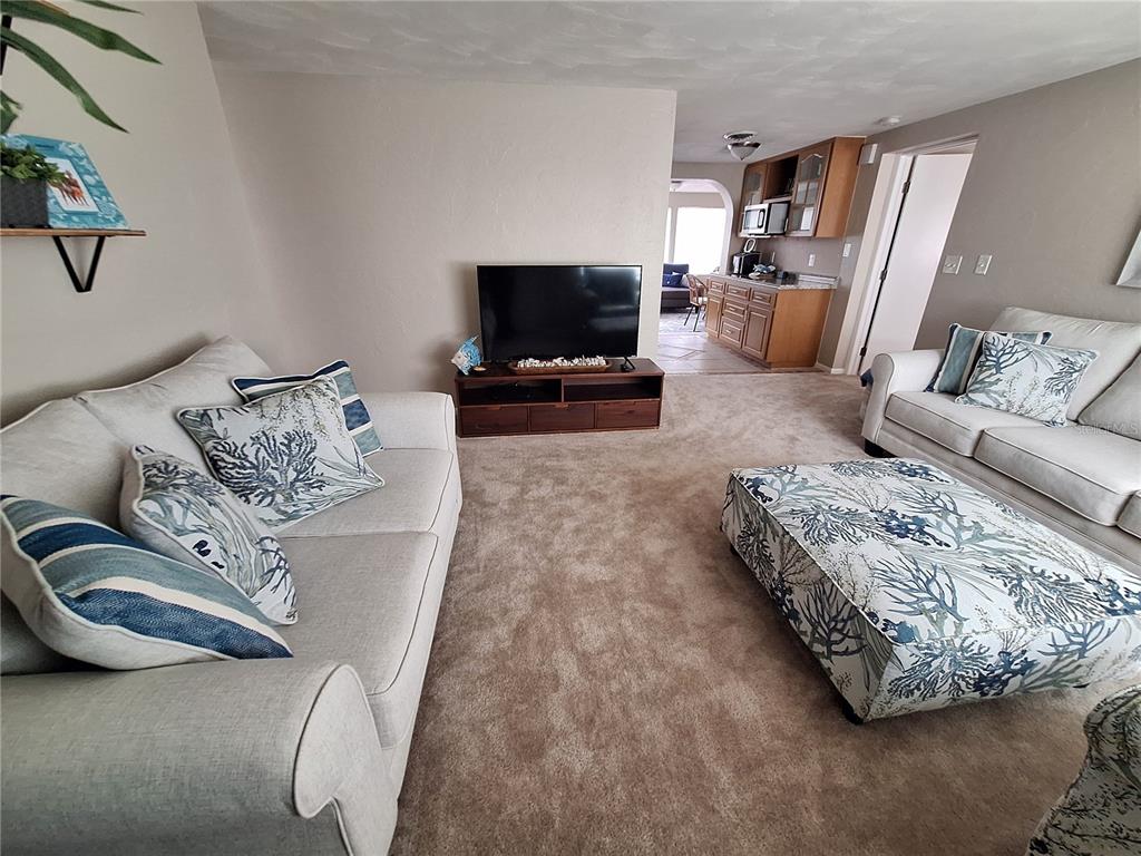 A living room features two beige sofas, a patterned ottoman, and a television on a stand — 858 E 7TH STREET, ENGLEWOOD, FL