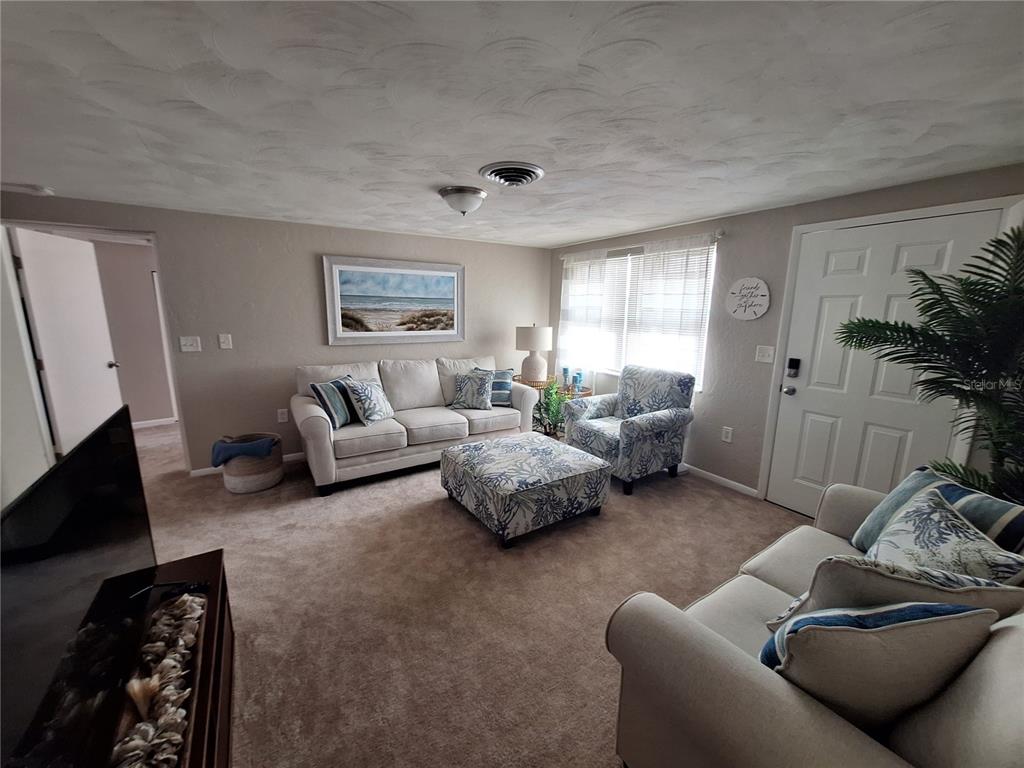 A living room features beige carpet, a light-colored sofa, patterned armchairs, and a matching ottoman — 858 E 7TH STREET, ENGLEWOOD, FL