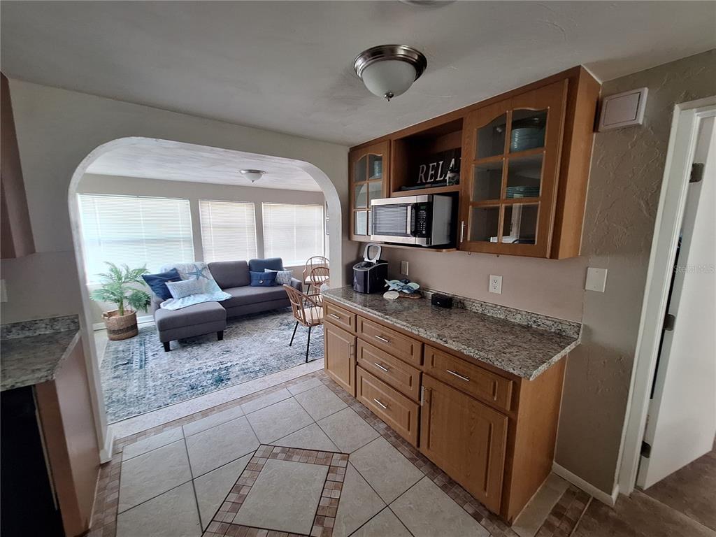 A kitchen with oak cabinets and granite countertops opens into a living room with tile flooring — 858 E 7TH STREET, ENGLEWOOD, FL