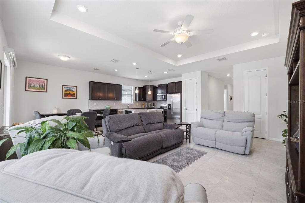 An open-concept living room and kitchen with dark cabinetry, light tile floors, and tray ceilings — 12929 PALAPA LOOP, SPRING HILL, FL