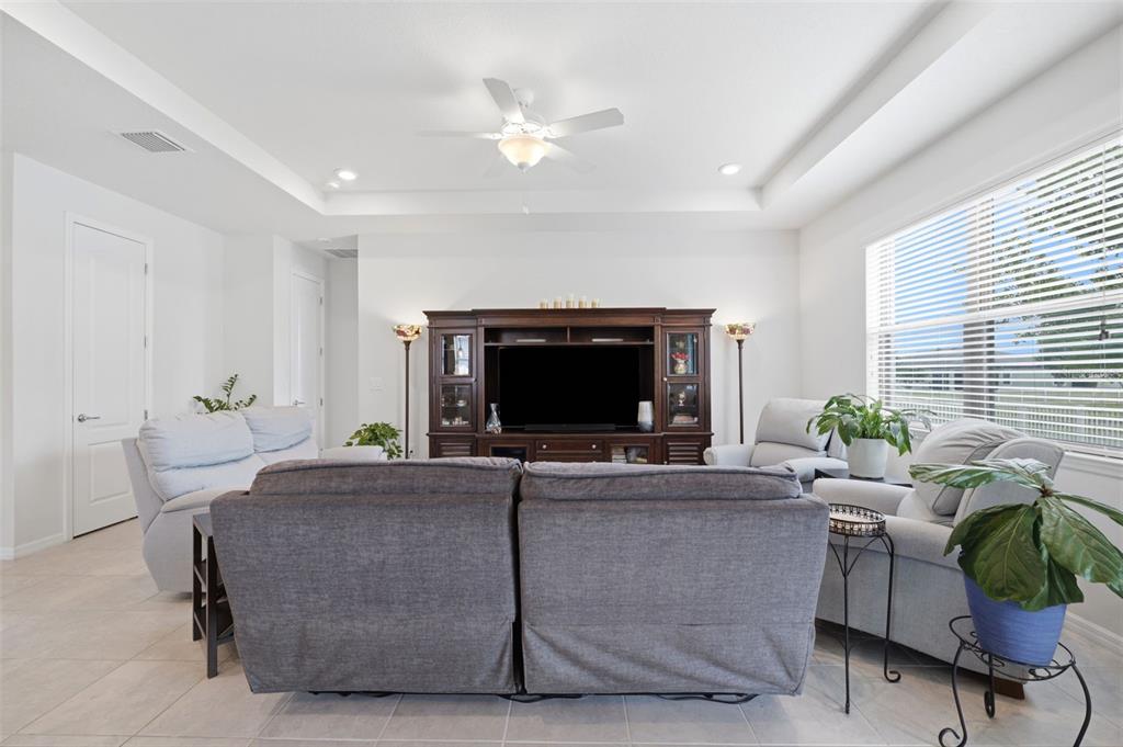 A living room features a dark wood entertainment center, gray sofas, and a ceiling fan — 12929 PALAPA LOOP, SPRING HILL, FL