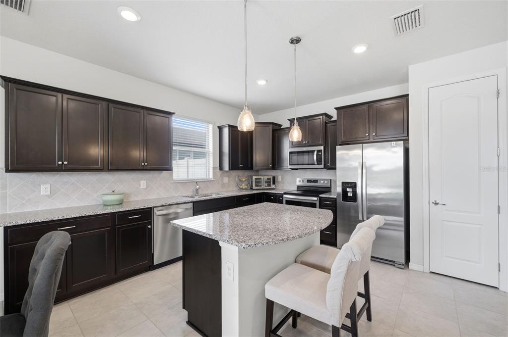 A kitchen features dark wood cabinets, granite countertops, stainless steel appliances, and a central island — 12929 PALAPA LOOP, SPRING HILL, FL